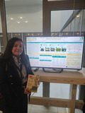 A woman standing next to a computer screen.
